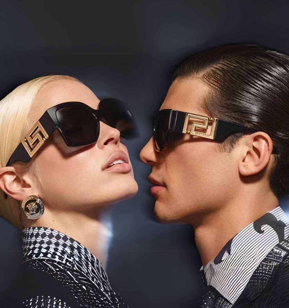 A brown-haired man and a blonde woman wearing Versace sunglasses featuring thick black frames and a bold gold logo